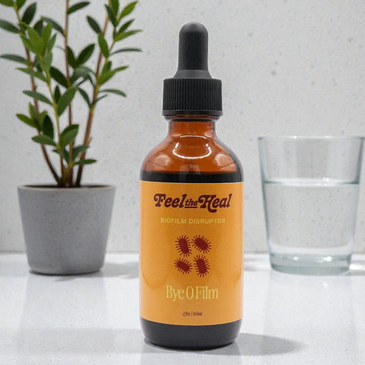 Bottle of 'Feel the Real' serum on a white surface with a plant and glass in the background