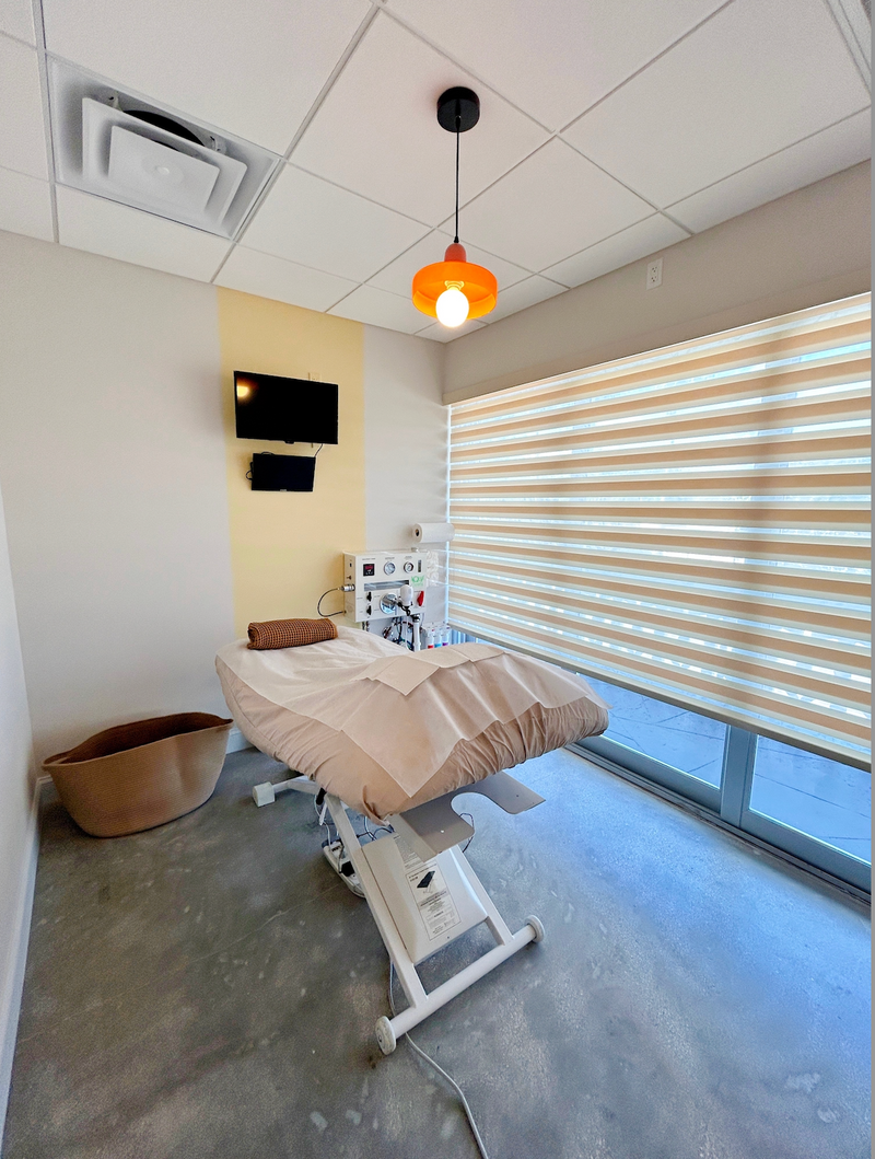 Medical examination room with a patient bed, television, and window blinds.colonic room at feel the heal