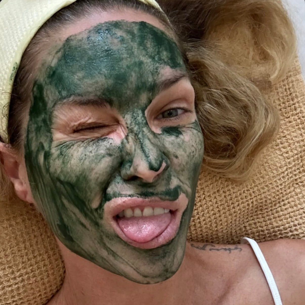 Person with a green facial mask on their face, lying on a textured surface.