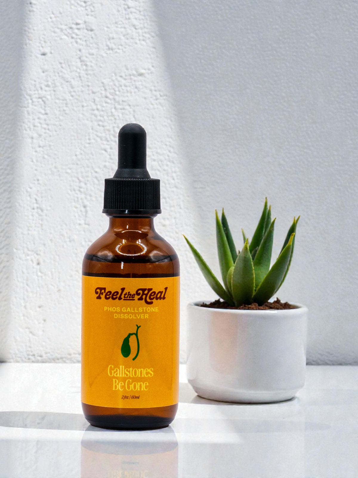 Bottle of 'Feel Heel' product with a dropper on a white surface next to a potted plant. for liver gallbladder cleanse