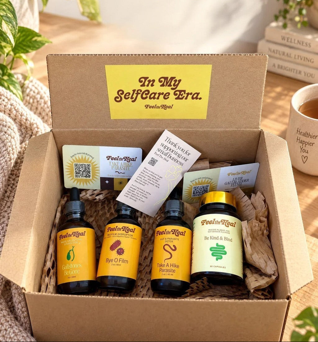 An open kraft gift box filled with wellness products from PaleoRoyal, including several small supplement bottles and cards, set on a wooden surface with a mug, books, and plants in a bright indoor setting.