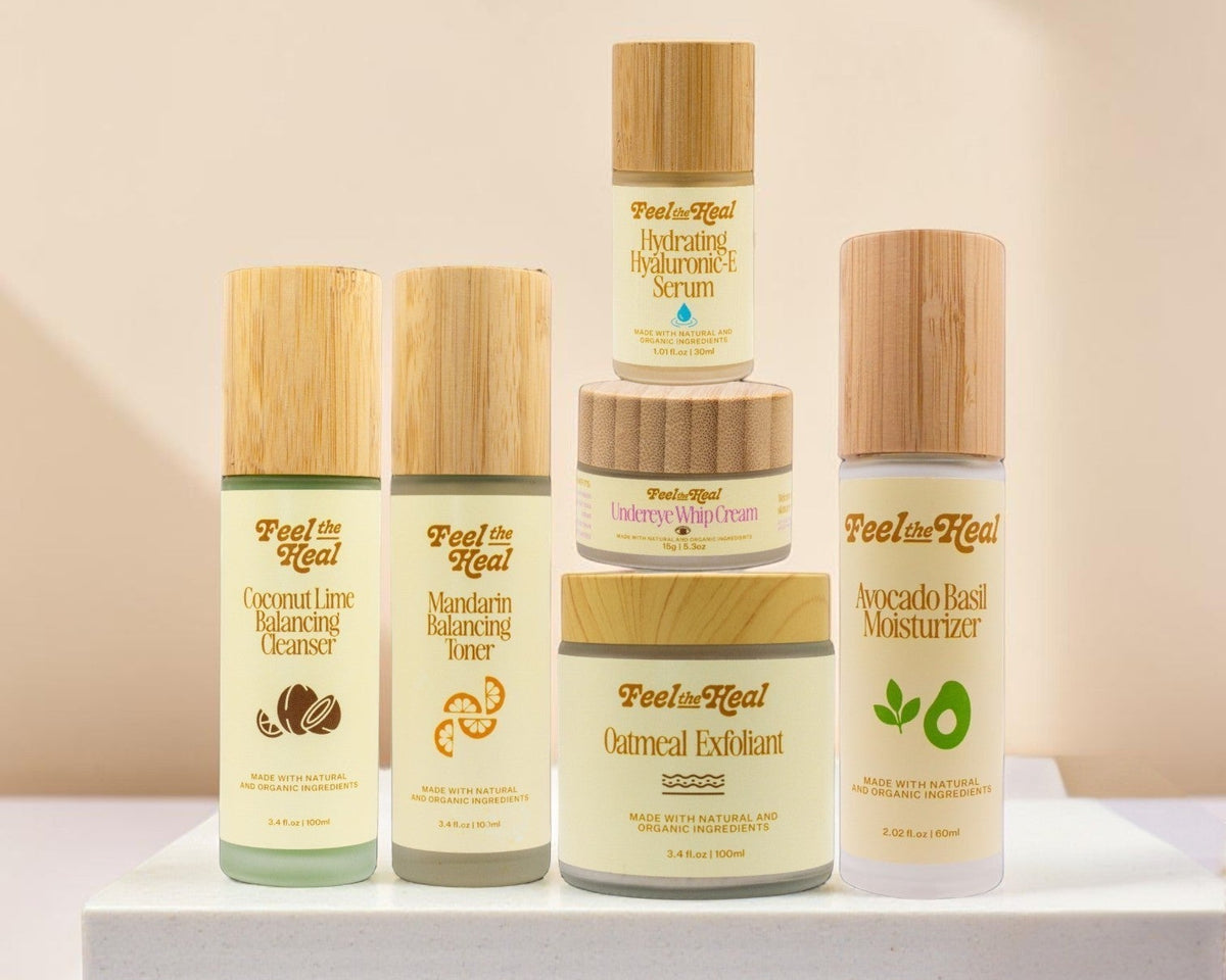 A set of five facial care products from Peony & Leaf arranged on a white pedestal against a warm beige background with soft diagonal shadows. The products include Coconut Lime Balancing Cleanser, Medium Balancing Serum, Oatmeal Exfoliant, and Avocado Reset Moisturizer, each with a light wood-textured cap and cream-colored labels.