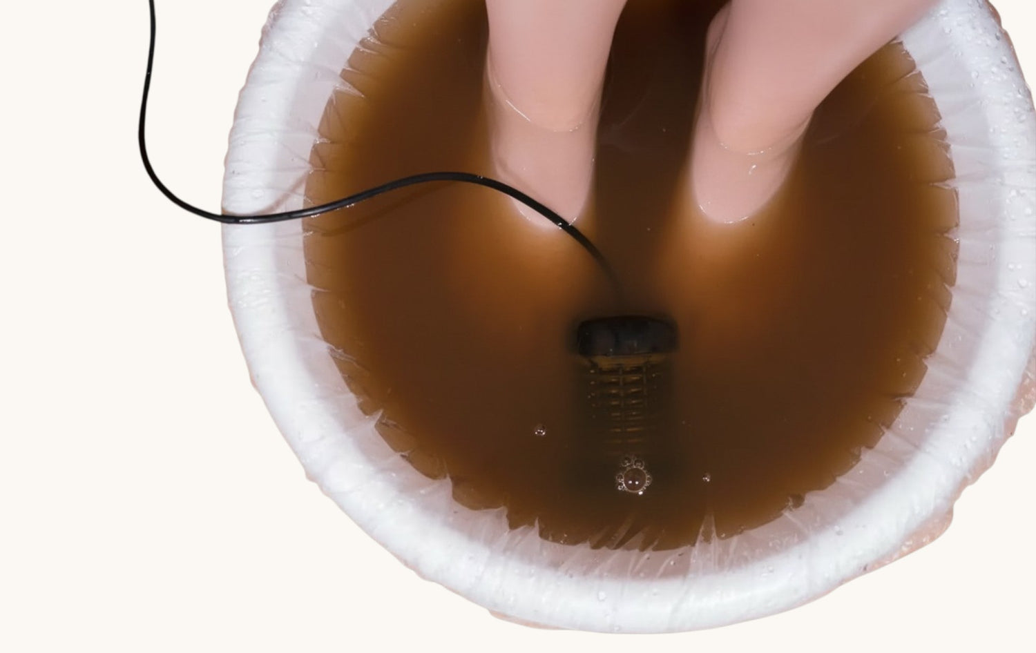 Close-up of a hand holding a black cord over a brown liquid in a white container.
