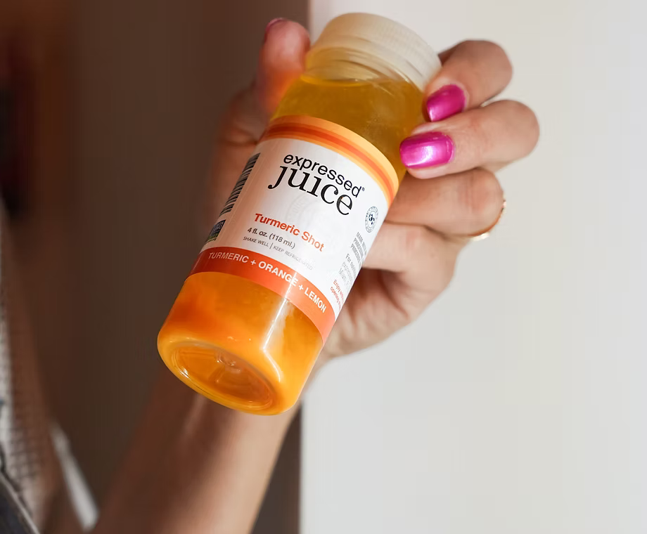 Hand holding a bottle of 'expressed juice' Turmeric Shot against a neutral background
