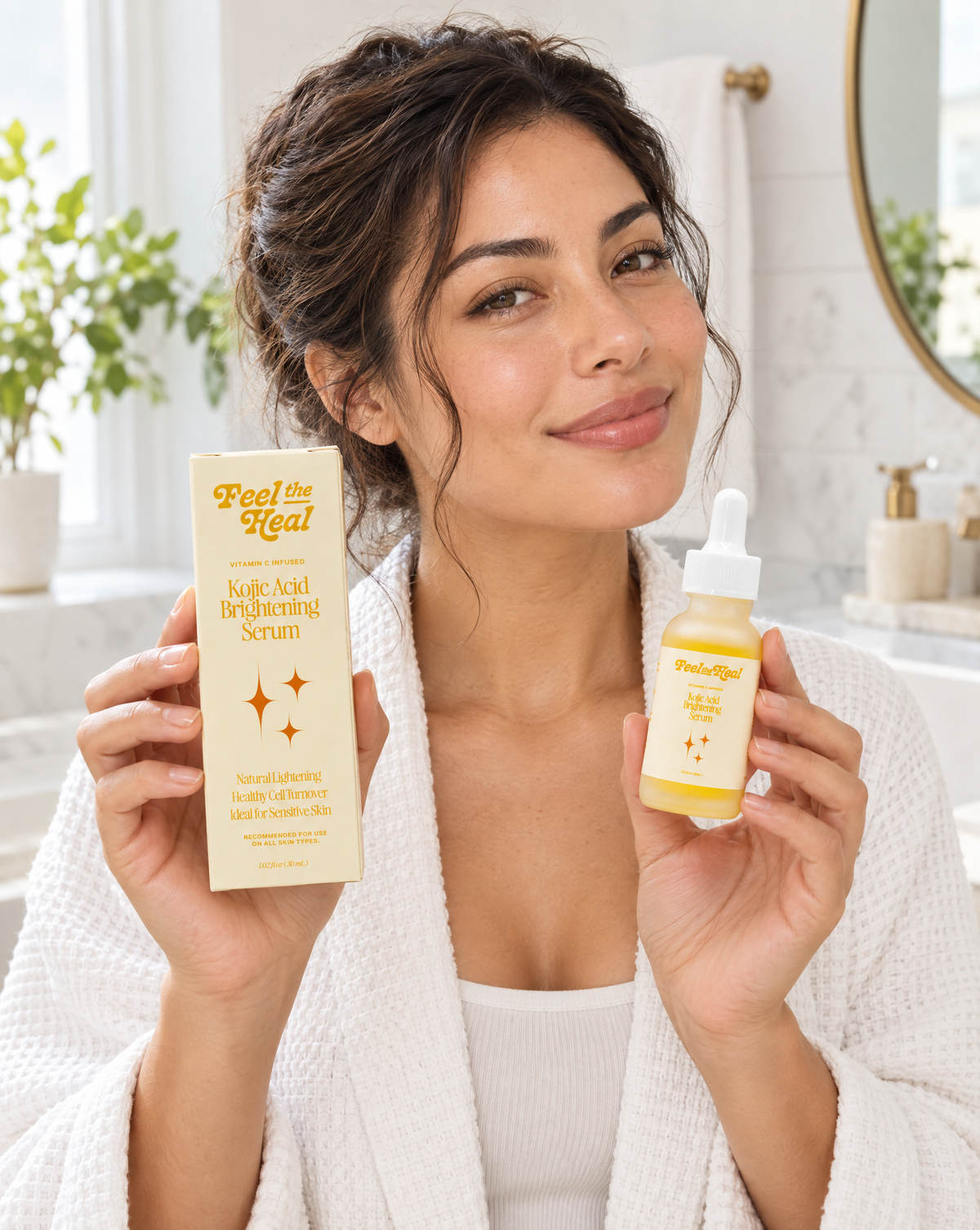 A woman in a white robe holds up a box and dropper bottle of 'Feel the Heal' Kojic Acid Brightening Serum in a bright bathroom setting.