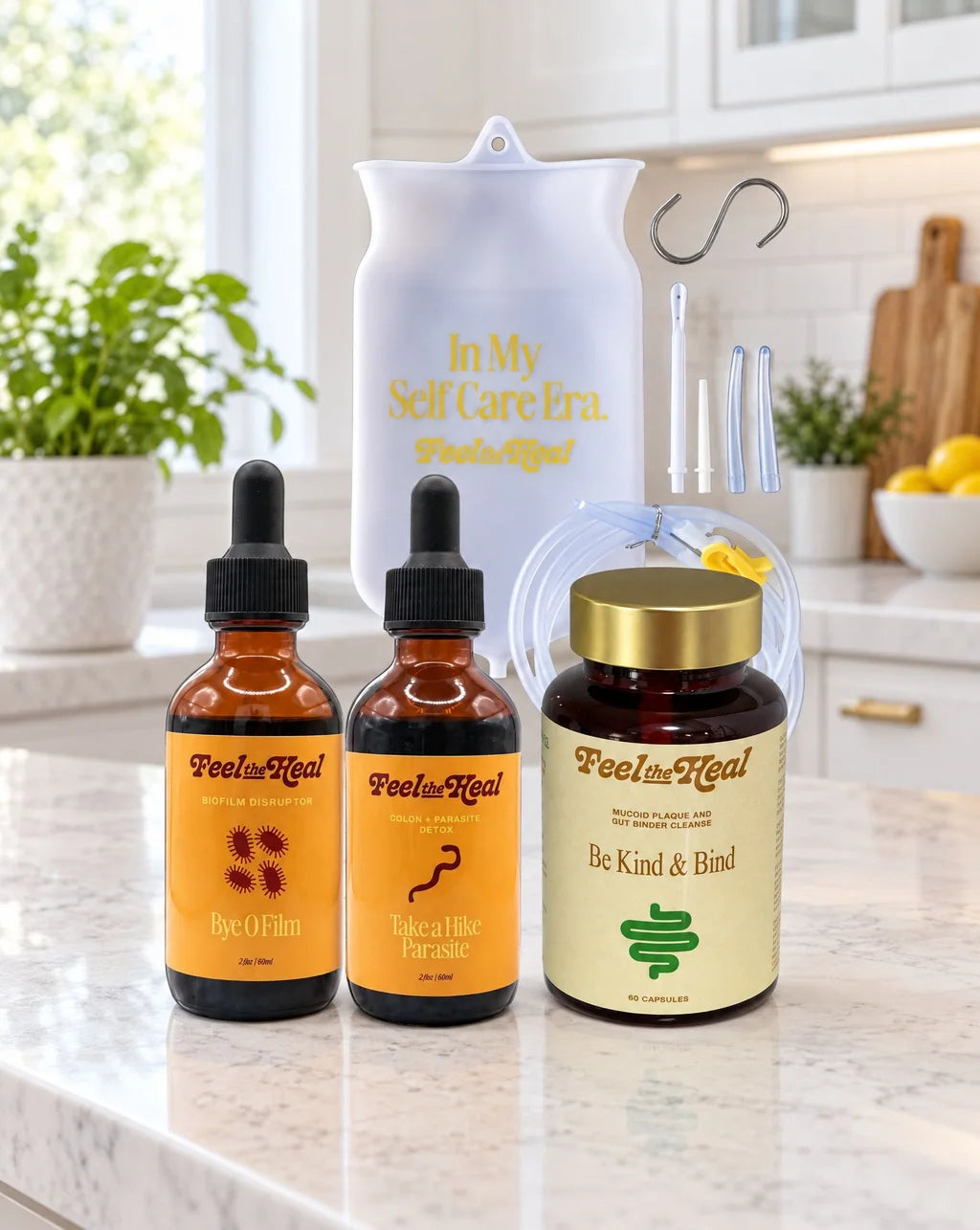 A feel the heal parasite kit wellness set on a marble countertop in a bright kitchen setting, featuring two amber dropper bottles, a supplement jar with a gold lid, a white silicone enema bag, and two glass applicator tubes.