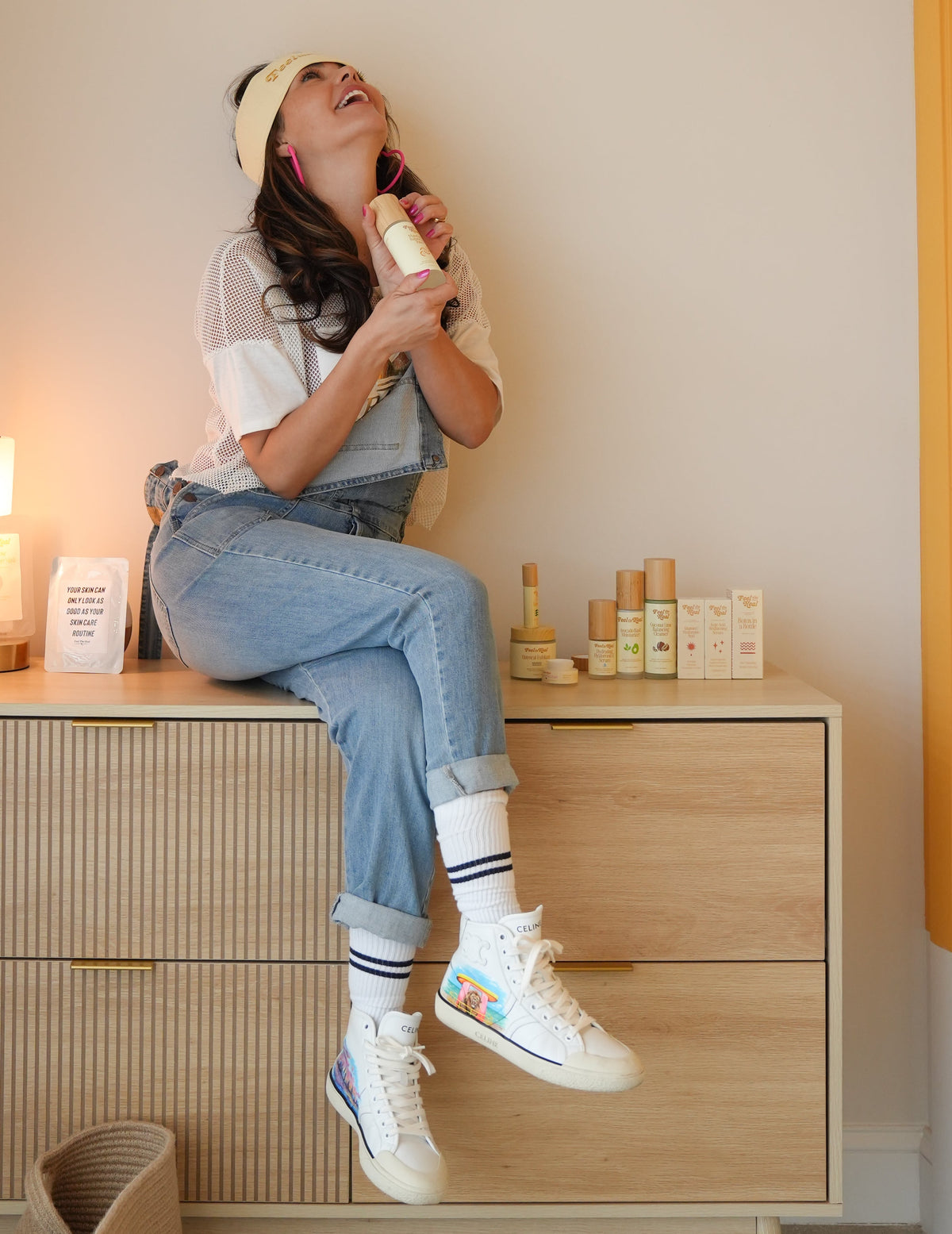 Person sitting on a wooden dresser in a room with yellow walls and a lamp.