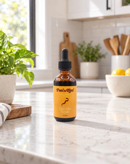 An amber glass dropper bottle labeled 'Feels Heal' and 'Immunity Herbs' standing on a white marble kitchen counter with a blurred kitchen background.