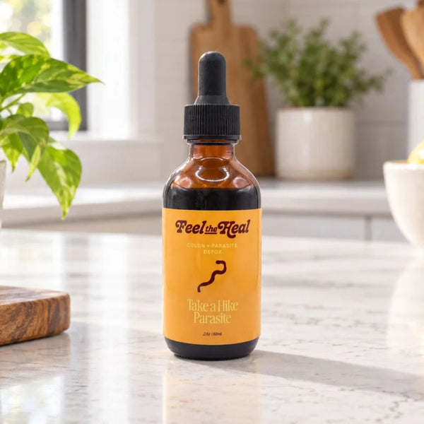 An amber glass dropper bottle labeled 'Feels Heal' standing on a white marble kitchen counter with a blurred kitchen background.