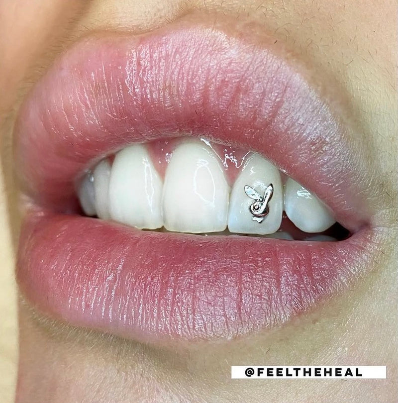 Close-up of a person's mouth with a small tattoo on the lower lip, featuring the brand 'Feel the Heal'.